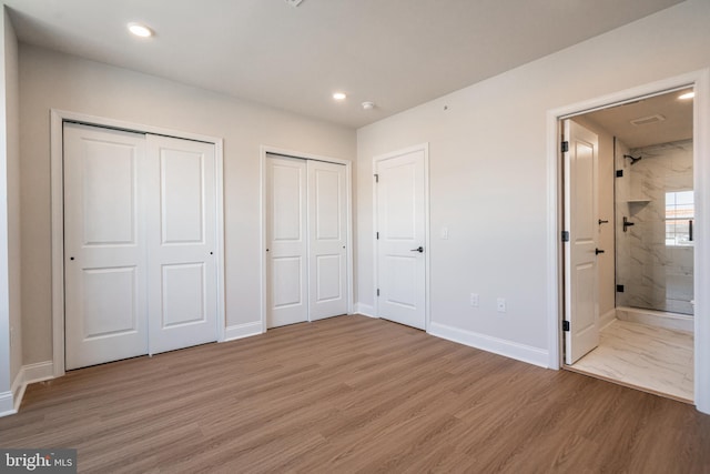 unfurnished bedroom with multiple closets, light wood-style floors, baseboards, ensuite bathroom, and recessed lighting