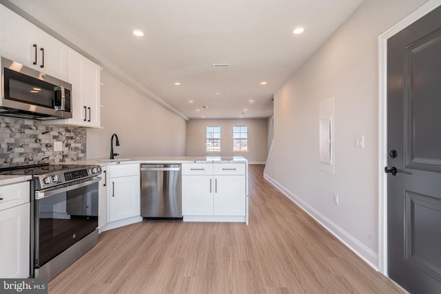 kitchen with appliances with stainless steel finishes, a peninsula, light wood-style flooring, white cabinets, and recessed lighting