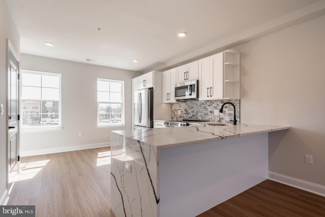 kitchen with appliances with stainless steel finishes, open shelves, light wood-style floors, light stone countertops, and recessed lighting