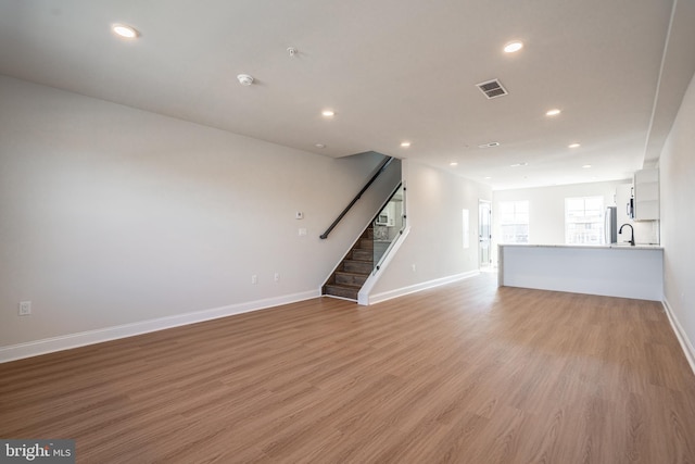 unfurnished living room with baseboards, light wood-style floors, stairway, recessed lighting, and a sink