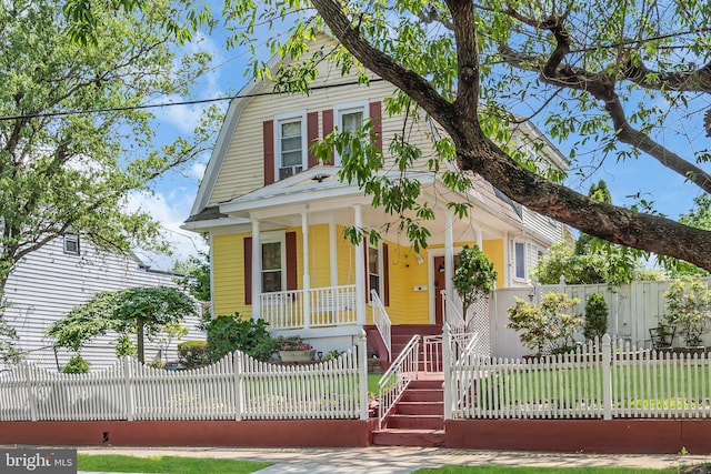 view of front of property with covered porch, a gambrel roof, and a fenced front yard