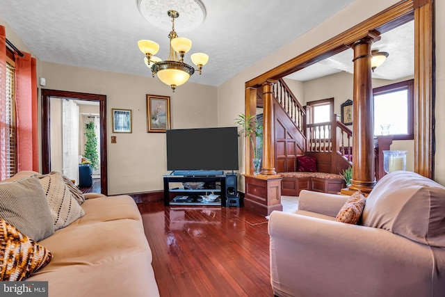 living area with ornate columns, a chandelier, hardwood / wood-style flooring, baseboards, and stairway
