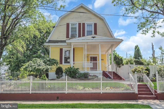 dutch colonial featuring a porch, a gambrel roof, a fenced front yard, and stairs