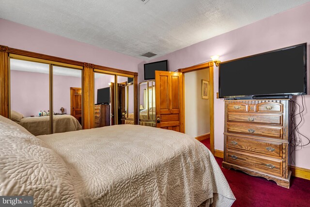 bedroom featuring dark colored carpet, baseboards, two closets, and a textured ceiling