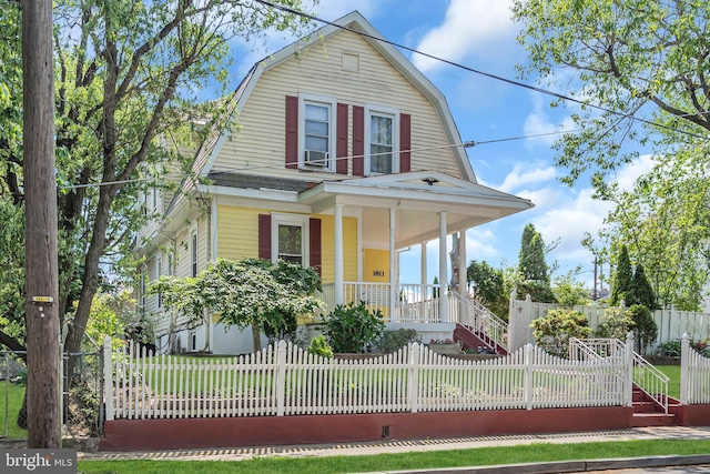 dutch colonial featuring a porch, a gambrel roof, and a fenced front yard
