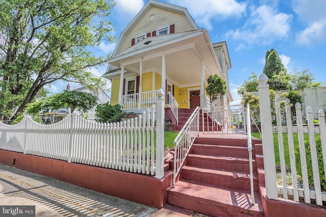 dutch colonial featuring a porch, a fenced front yard, a gambrel roof, and stairway