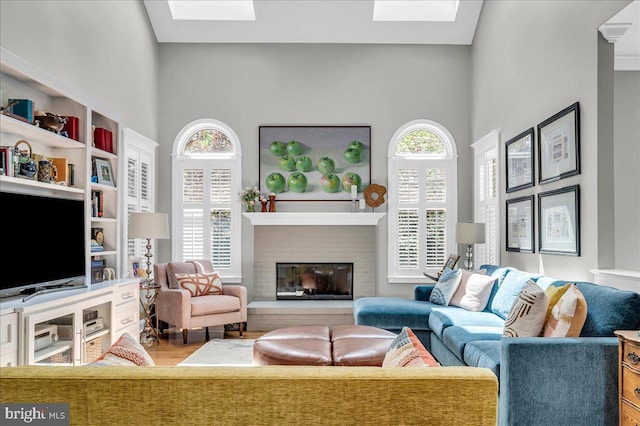 living room with a skylight, healthy amount of natural light, a brick fireplace, wood finished floors, and a towering ceiling