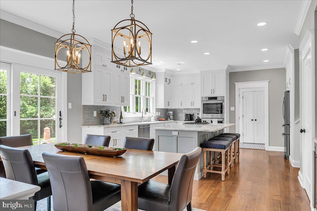 dining area with a chandelier, ornamental molding, recessed lighting, wood finished floors, and baseboards