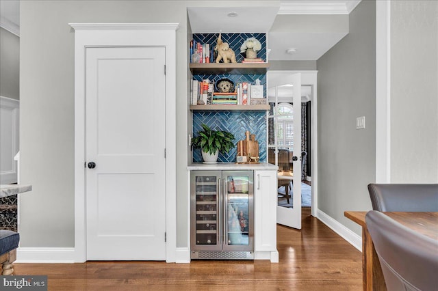 indoor dry bar with beverage cooler, wood finished floors, ornamental molding, and baseboards