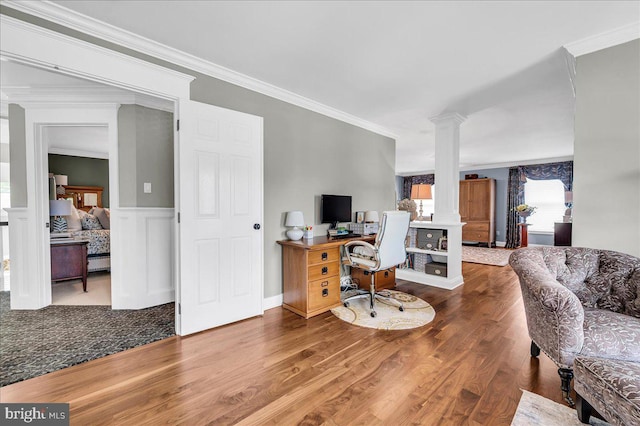 office space featuring ornate columns, crown molding, wood finished floors, and a wainscoted wall