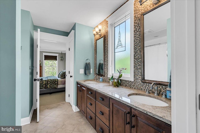 ensuite bathroom featuring double vanity, tile patterned floors, baseboards, and backsplash