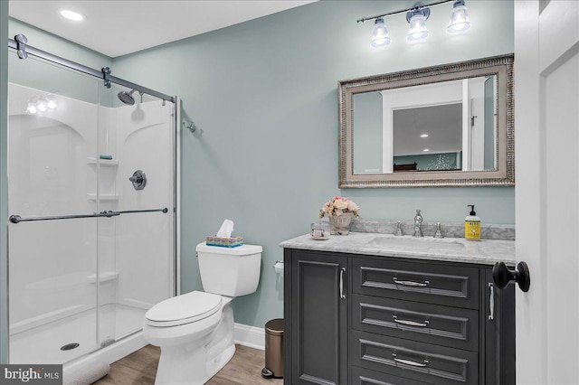 bathroom with toilet, a stall shower, wood finished floors, vanity, and baseboards