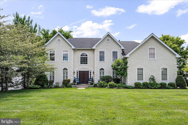 georgian-style home featuring a front yard and a shingled roof