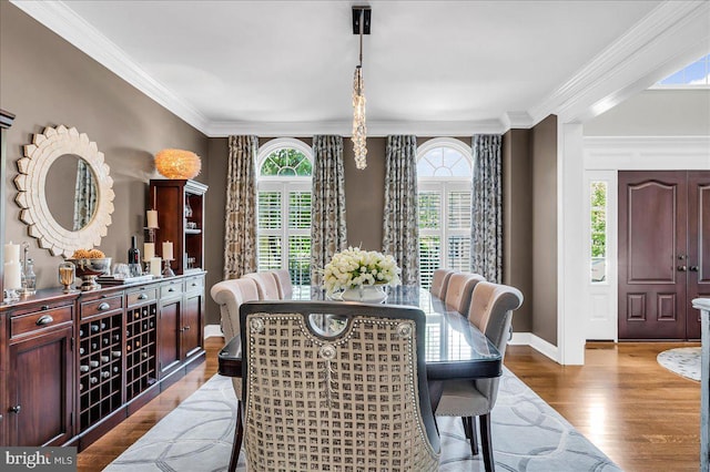 dining space featuring healthy amount of natural light, wood finished floors, crown molding, and baseboards