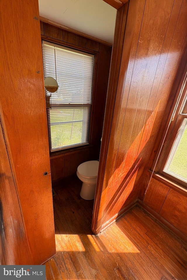 bathroom with hardwood / wood-style floors, wood walls, toilet, and plenty of natural light
