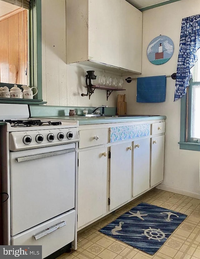 kitchen featuring white gas range oven, white cabinets, and light countertops