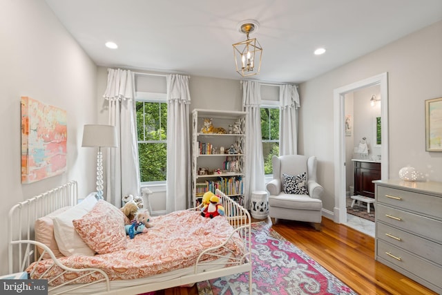 bedroom featuring wood finished floors, recessed lighting, ensuite bathroom, baseboards, and a chandelier