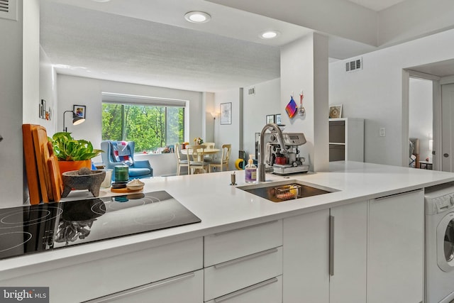 2141 Wisconsin Ave NW Unit 103, Washington, DC 20007 - kitchen with washer / dryer, a sink, black electric stovetop, light countertops, and recessed lighting