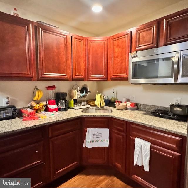 9330 China Grove Ct, Manassas, VA 20110 - kitchen with stainless steel microwave, light wood finished floors, light stone countertops, reddish brown cabinets, and recessed lighting