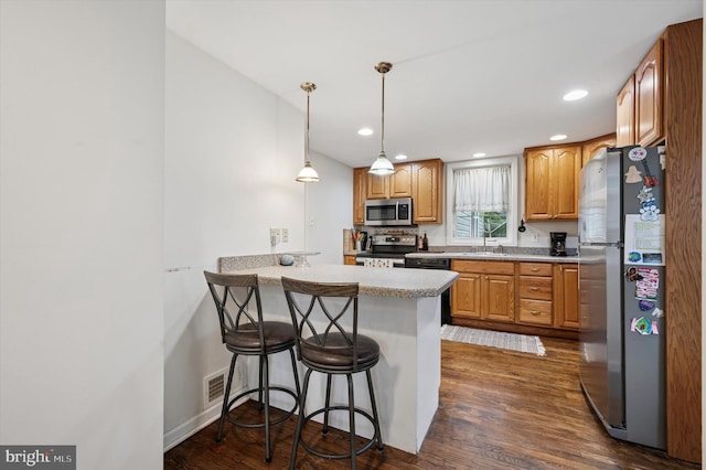 kitchen featuring stainless steel appliances, a sink, dark wood-style flooring, a breakfast bar, and a peninsula