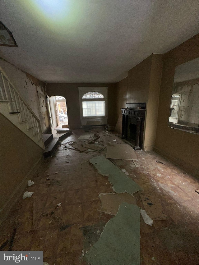 unfurnished living room featuring arched walkways, a fireplace, and stairs