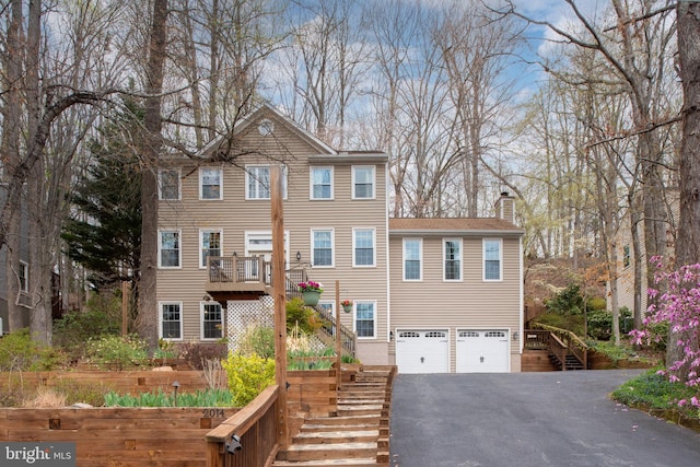 view of front of home with stairs, an attached garage, asphalt driveway, and a chimney