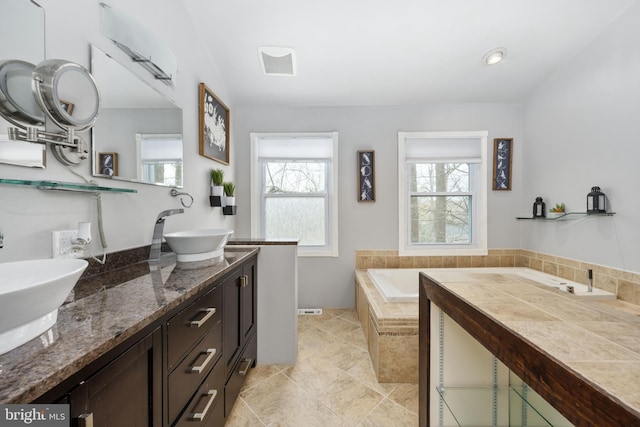 full bathroom with double vanity, tiled tub, and tile patterned floors