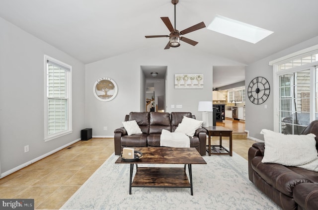living room with plenty of natural light, ceiling fan, a skylight, baseboards, and lofted ceiling