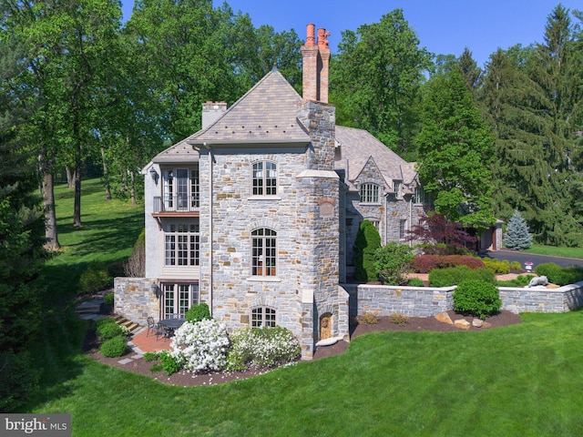 view of side of home featuring a high end roof, a chimney, a lawn, and stone siding