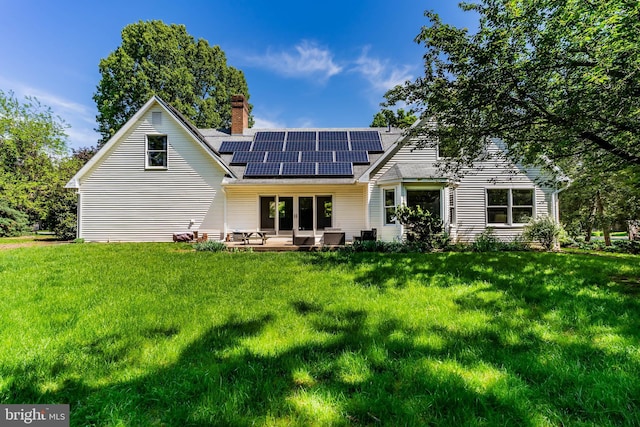 rear view of property with roof with shingles, roof mounted solar panels, a chimney, and a yard