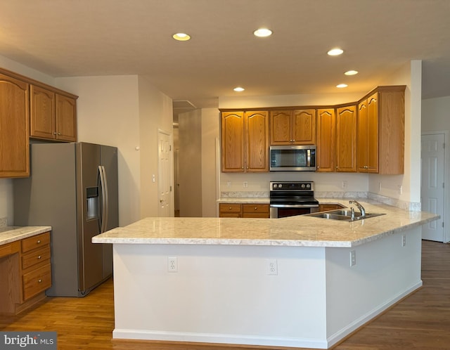 kitchen featuring appliances with stainless steel finishes, a sink, a peninsula, wood finished floors, and light countertops