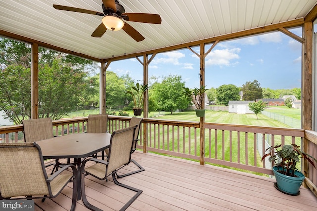 wooden deck with outdoor dining space, a ceiling fan, and view of scattered trees