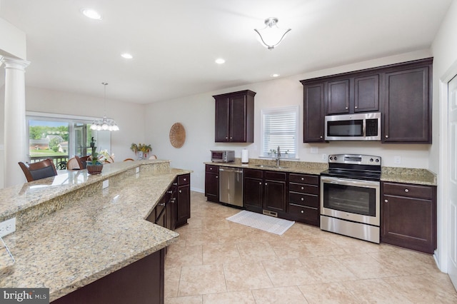 kitchen featuring appliances with stainless steel finishes, a sink, dark brown cabinetry, light stone countertops, and decorative columns