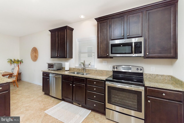 kitchen featuring stainless steel appliances, a sink, dark brown cabinetry, light stone countertops, and recessed lighting