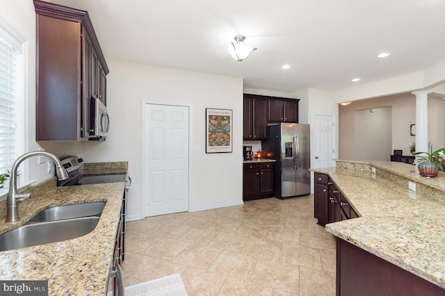 kitchen featuring appliances with stainless steel finishes, a sink, light stone counters, dark brown cabinetry, and decorative columns