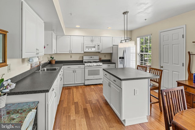 kitchen featuring white appliances, a sink, dark countertops, white cabinets, and light wood-style flooring