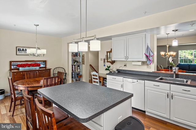 kitchen with a chandelier, white dishwasher, dark countertops, a sink, and wood finished floors