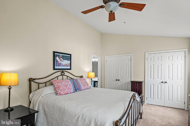 bedroom with vaulted ceiling, light colored carpet, two closets, and a ceiling fan