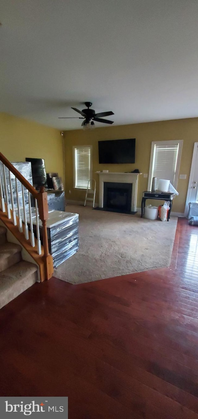 living area with wood finished floors, stairs, a fireplace, and ceiling fan