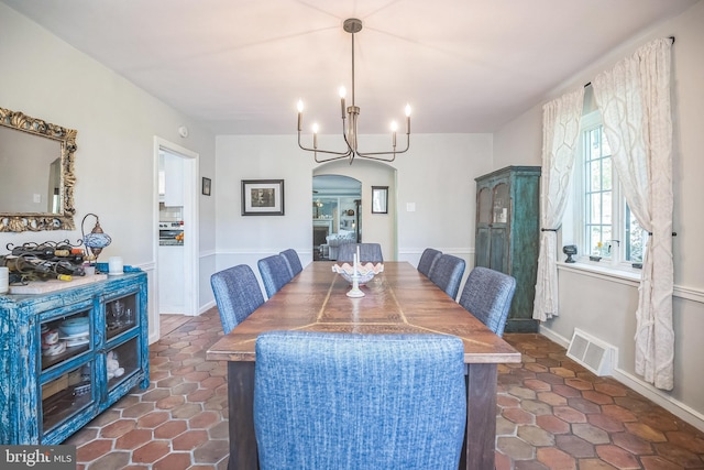 dining space featuring arched walkways, a chandelier, baseboards, and dark tile patterned flooring