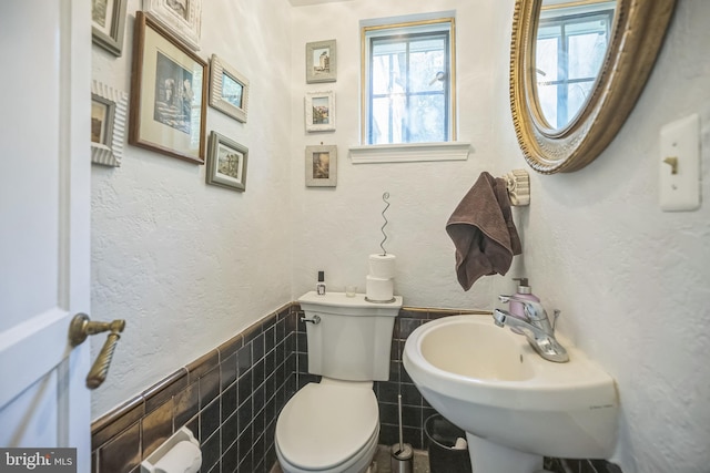 half bathroom with toilet, tile walls, a wainscoted wall, and a sink
