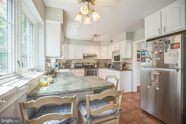 kitchen with appliances with stainless steel finishes, under cabinet range hood, a sink, tasteful backsplash, and tile patterned floors