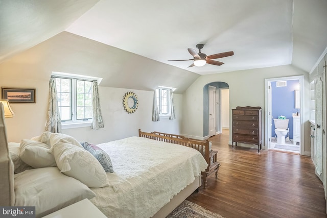 bedroom with vaulted ceiling, dark wood-style floors, multiple windows, arched walkways, and connected bathroom