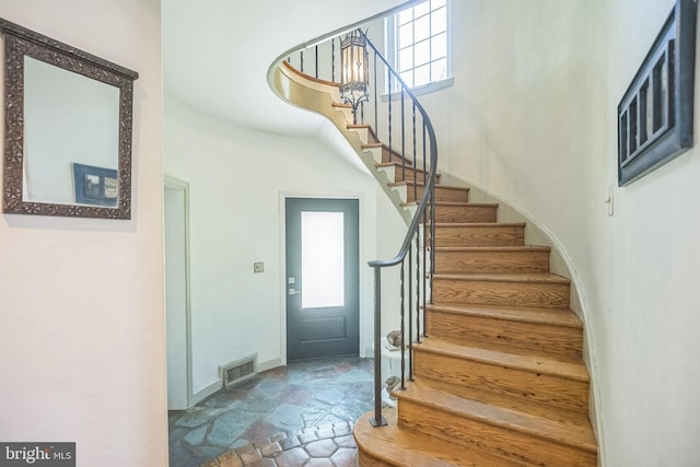 stairs featuring stone finish flooring, a towering ceiling, and baseboards