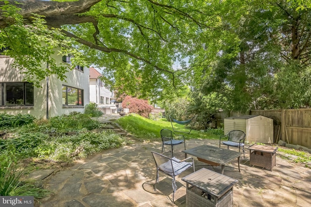 view of patio with a storage shed, an outbuilding, fence, and an outdoor fire pit