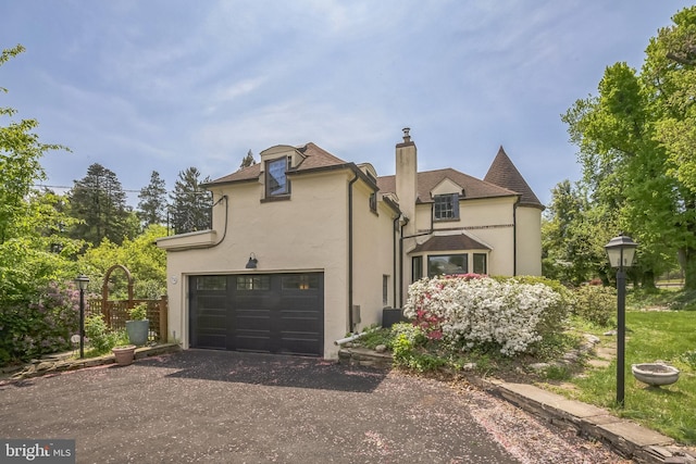 view of front of home featuring stucco siding, a chimney, asphalt driveway, and a garage