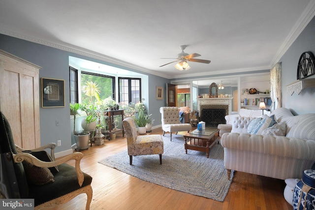living room featuring ornamental molding, wood finished floors, ceiling fan, baseboards, and a fireplace