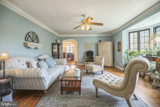 living area with arched walkways, wood finished floors, ceiling fan, crown molding, and baseboards
