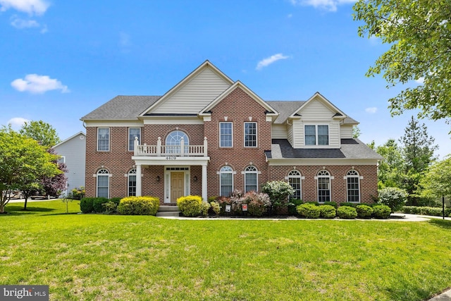 colonial house with brick siding, a front yard, and a balcony