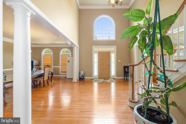 foyer featuring ornamental molding, light wood-style flooring, healthy amount of natural light, stairway, and ornate columns